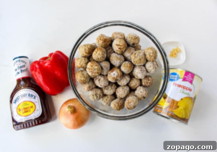 Effortless BBQ Meatballs 3 A bowl of frozen meatballs, perfect for Slow Cooker BBQ Meatballs, is surrounded by a bottle of barbecue sauce, a red bell pepper, an onion, a can of pineapple chunks, and minced garlic on a white surface, ready for assembly.
