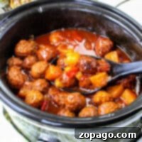 Slow cooker BBQ meatballs and pineapple chunks swim in a tangy red sauce, with a ladle resting inside. Pineapple peeks from the background, promising that sweet and savory magic awaits.