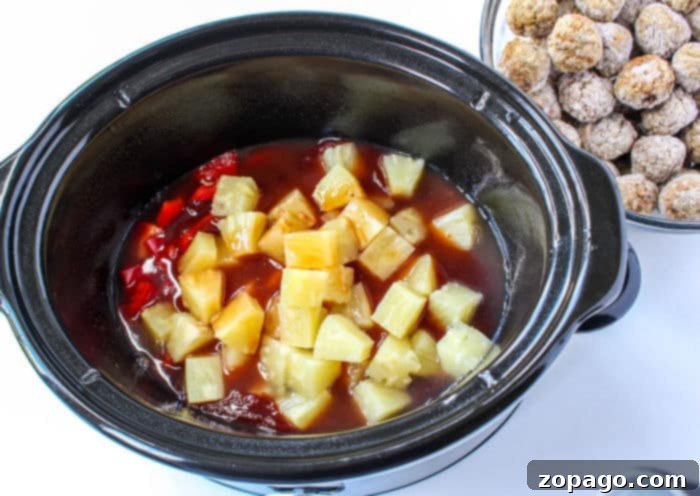 Effortless BBQ Meatballs 6 A slow cooker brimming with a tangy red sauce spiced with diced pineapples and red peppers. Beside it, on the pristine white surface, rests a bowl of uncooked BBQ meatballs, ready to transform into savory delights.