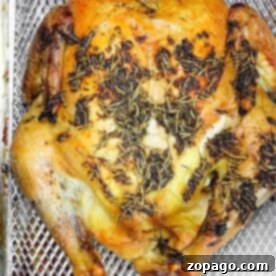 Oven Baked Frozen Chicken 6 Whole roasted chicken with herbs on top, served in a roasting pan, a delicious outcome of cooking a frozen chicken in the oven.