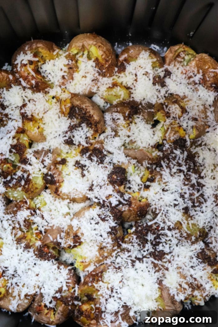 Air-fried smashed potatoes in a black pan, topped with melted cheese and toasted breadcrumbs, ready to serve.