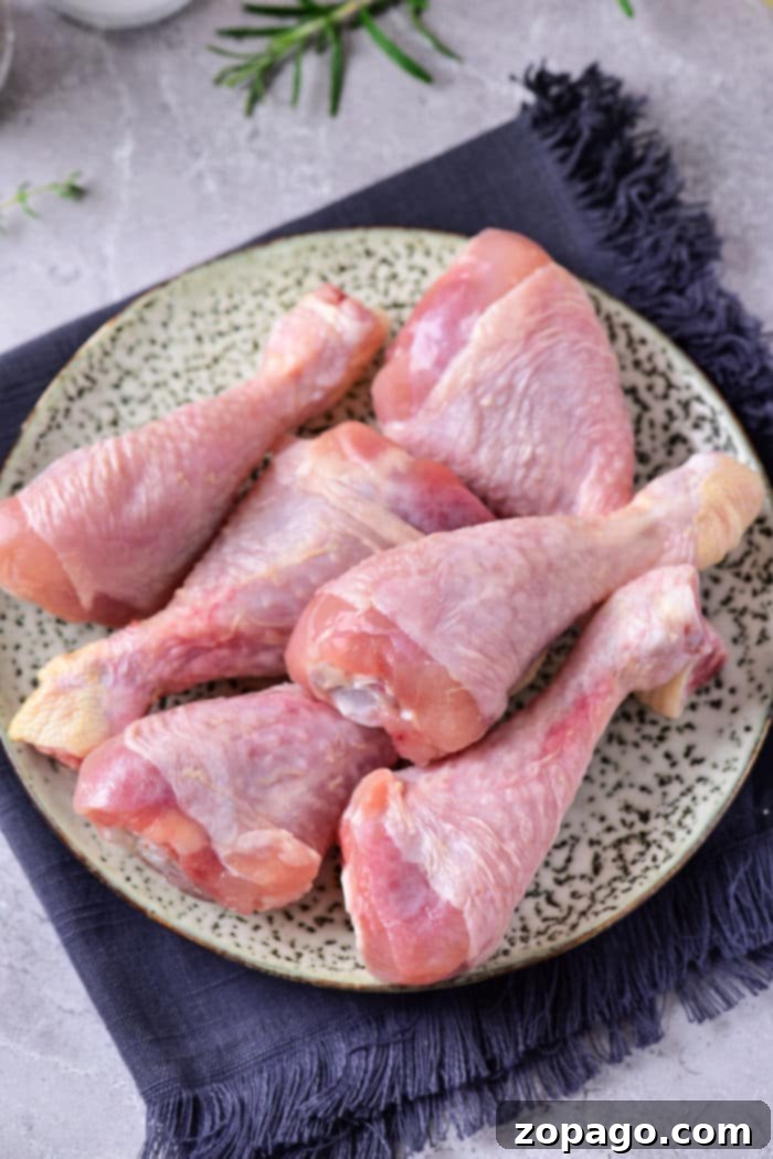 Microwave Chicken Thawing Made Easy 8 Raw chicken drumsticks on a speckled plate, ready to be seasoned after learning how to defrost chicken in the microwave, rest on a dark fabric napkin.
