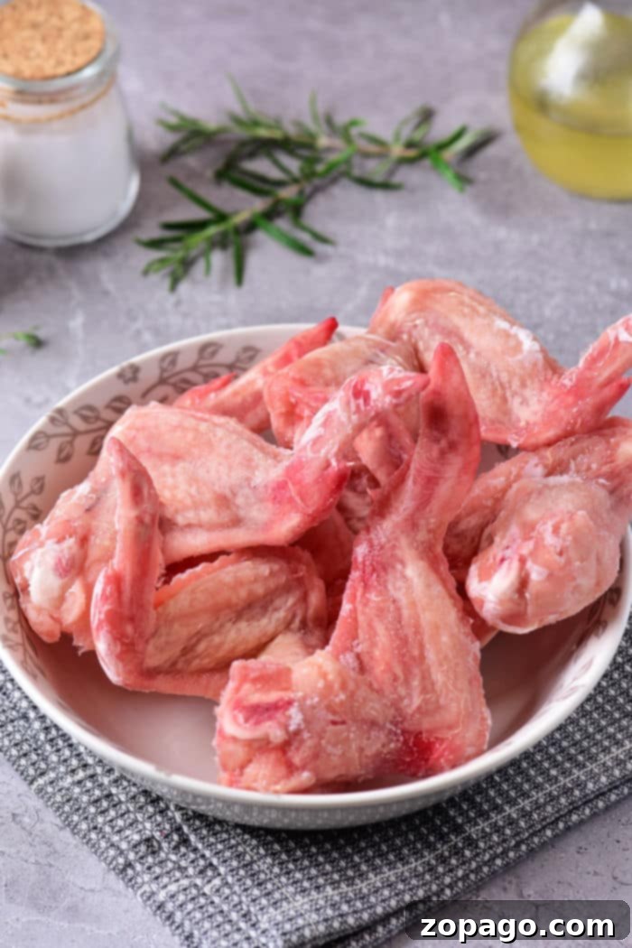Microwave Chicken Thawing Made Easy 9 A bowl of raw chicken wings sits on a gray kitchen cloth adorned with fresh rosemary, oil, and a jar of salt in the background. Discover how to defrost chicken in the microwave to prepare your feast quickly and efficiently.