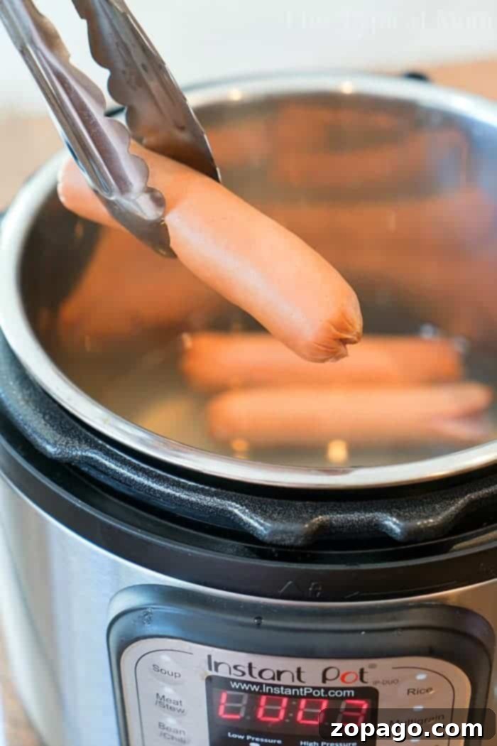 Perfectly Simmered Franks 5 Tongs are holding a hot dog over an open Instant Pot, which is filled with hot dogs. The digital display on the Instant Pot shows a reading of "0003," indicating how long to boil hot dogs for perfectly cooked results every time.
