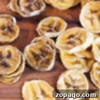 A close-up of sliced banana chips, expertly dehydrated, scattered on a rustic wooden surface.