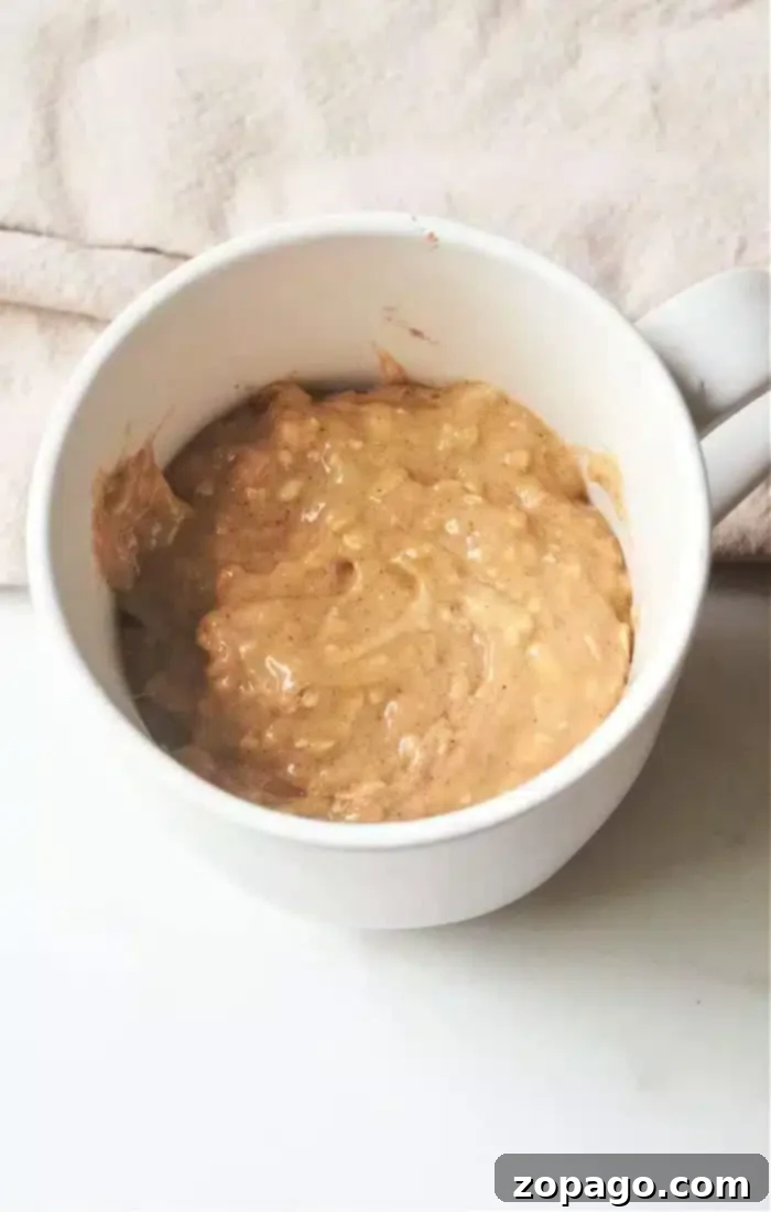 Microwave Banana Bread Bliss 4 A white mug holds a thick mixture of mashed bananas and peanut butter, reminiscent of banana bread in a mug, sitting on a white surface with a beige cloth in the background.