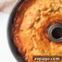 A golden brown Banana Bread Bundt Cake rests elegantly in a baking pan, with a light cloth draped softly in the background.