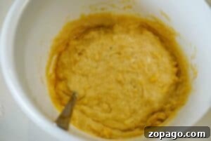 Thick yellow batter for banana bread with mayonnaise being mixed in a white bowl with a metal spoon.