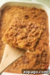 Close-up of a crumbly banana coffee cake slice on a wooden spatula above the rest in a baking dish.