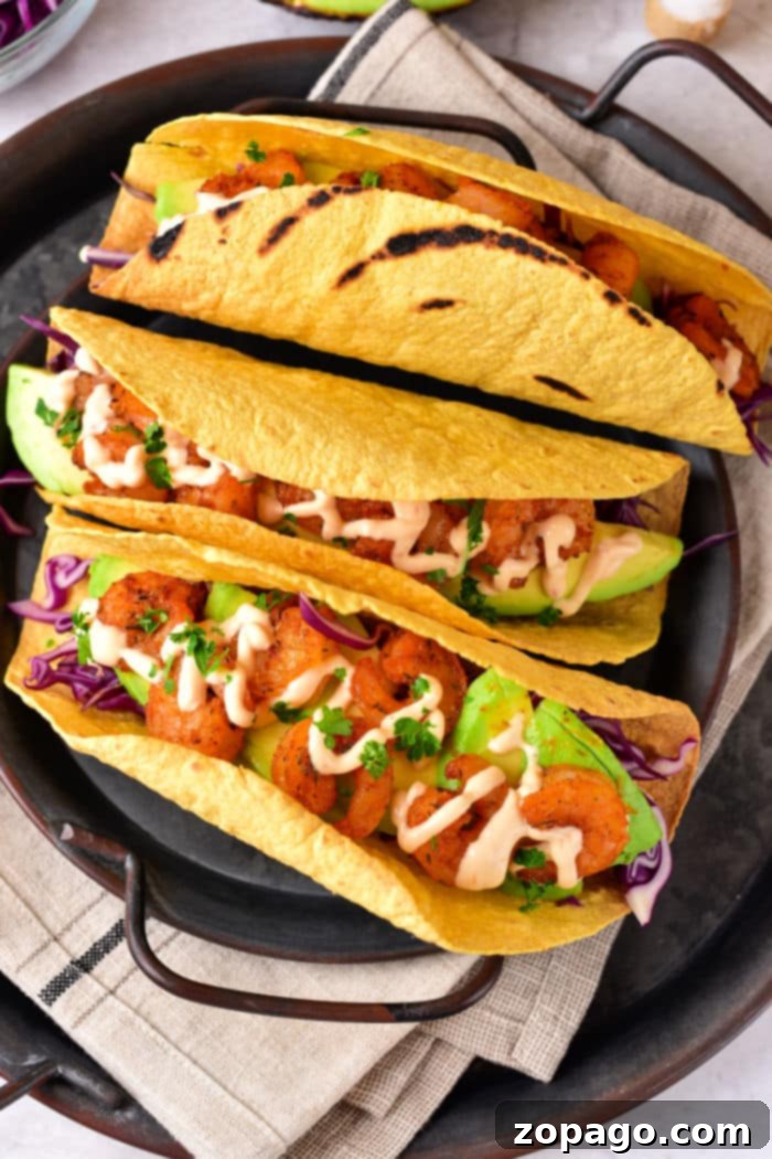 Crispy Air Fryer Taco Shells 2 Three shrimp tacos with avocado, purple cabbage, and sauce nestled in air-fried corn tortilla shells on a black platter.