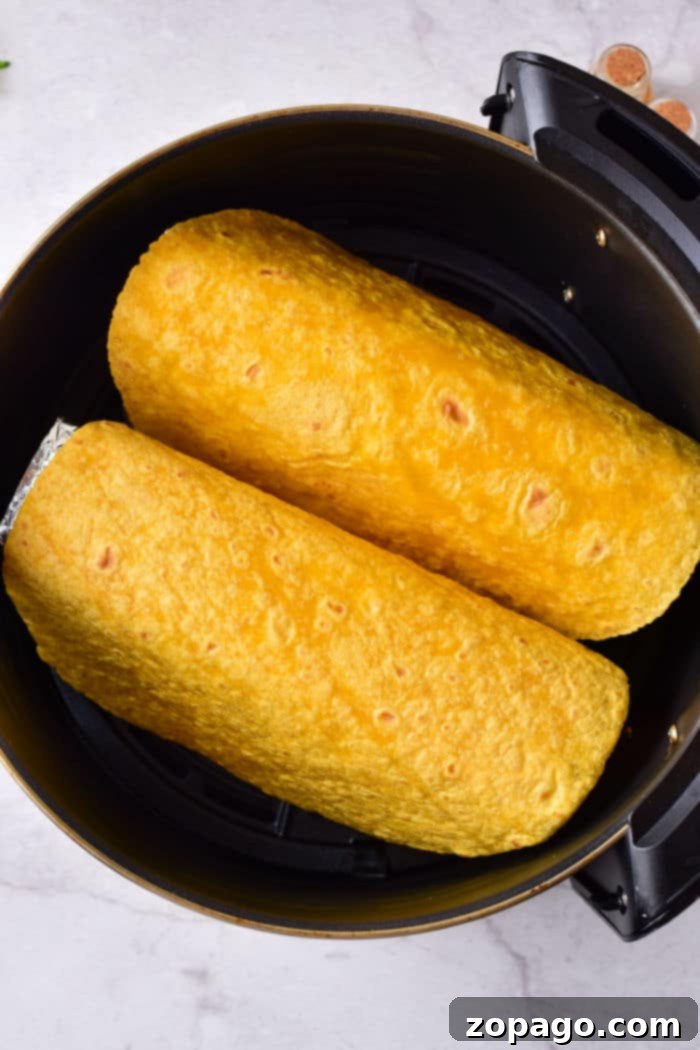 Crispy Air Fryer Taco Shells 5 Two yellow tortilla shells wrapped around delicious fillings, nestled side by side in a black cooking pot, reminiscent of taco shells prepared perfectly in an air fryer.