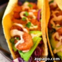 Close-up of two shrimp tacos with avocado slices, red cabbage, and creamy sauce in corn tortillas. Discover how to make shrimp tacos with frozen cooked shrimp for a quick and delightful meal option.