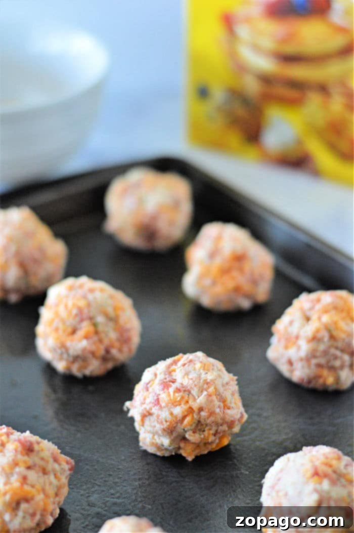 Golden Bisquick Sausage Bites 4 Unbaked sausage balls rest on a black baking sheet, with a cereal box subtly visible in the background, reminiscent of simplicity, much like crafting Bisquick sausage balls with just 3 ingredients.