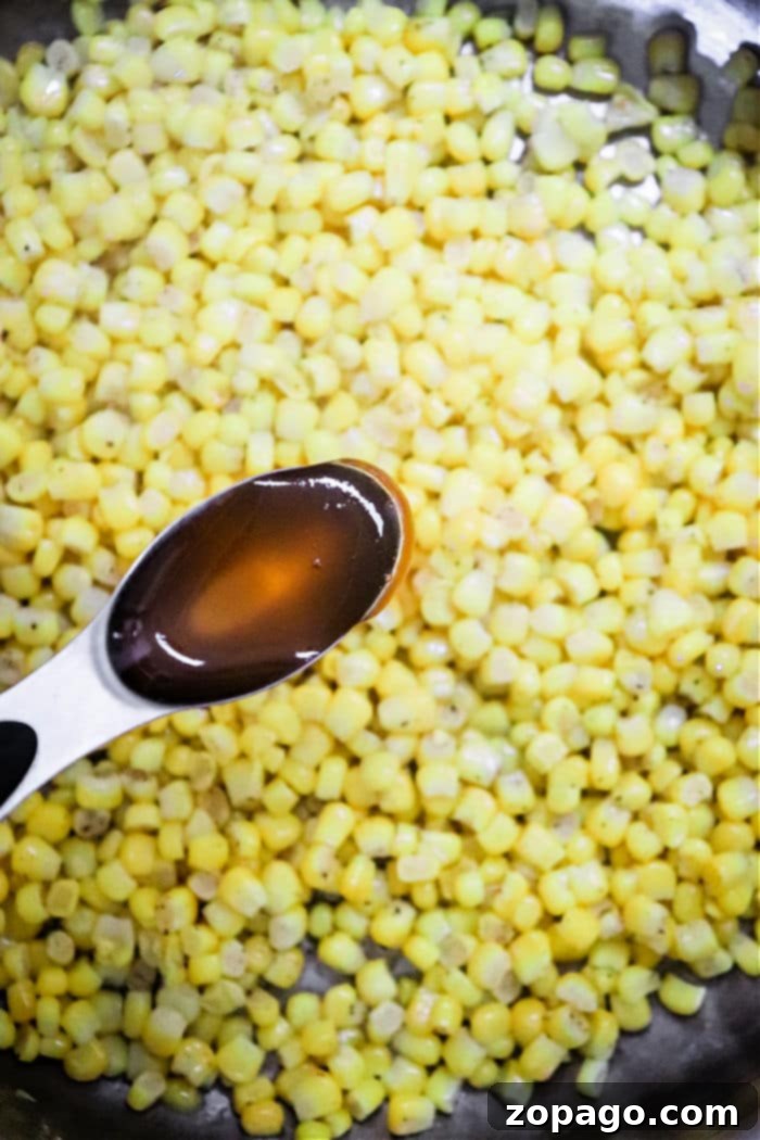 Golden Honey Butter Skillet Corn 5 A spoon with honey hovers above a skillet of Honey Butter Skillet Corn, perfectly sautéed for a deliciously sweet and savory dish.