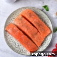 Three raw sockeye salmon fillets rest on a plate with spices, surrounded by cream, mushrooms, cherry tomatoes, and herbs—perfect for learning how to cook sockeye salmon with the finest accompaniments.
