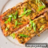 Plate with two slices of salmon topped with a rich mustard sauce and garnished with sliced green onions. A fork is on the side.