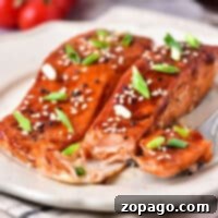 Air fryer Teriyaki salmon fillets on a plate, topped with sesame seeds and green onions, surrounded by cherry tomatoes.