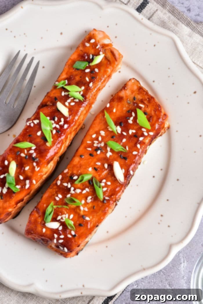 Sticky Air Fryer Teriyaki Salmon 8 Teriyaki salmon air fried to perfection, sprinkled with sesame seeds and green onions, elegantly presented on a white plate alongside a fork for a healthy and easy dinner.