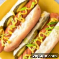Two hot dogs with pickles, mustard, and green onions rest on a yellow plate. Want them quick? Here's a tip: learn how long to cook hot dogs in the microwave for perfectly heated bites.