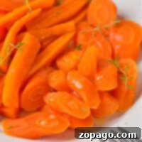 A plate of sliced and whole cooked carrots, perfectly tender from the microwave, is garnished with fresh herbs, with a fork on the side.