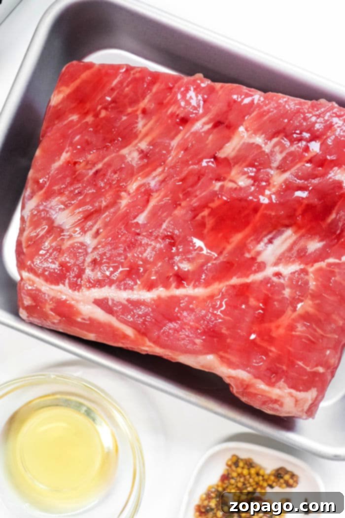 Perfect Air Fryer Corned Beef 3 Raw corned beef brisket in a silver pan, surrounded by oil and spices, ready for air frying.