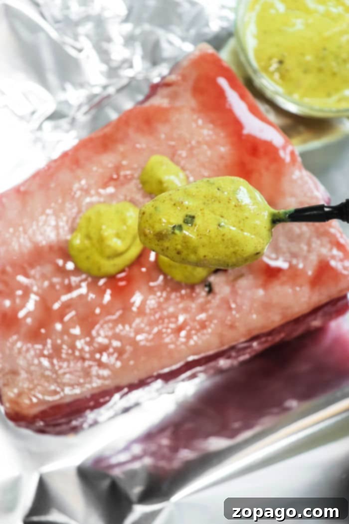 Perfect Air Fryer Corned Beef 4 A slab of corned beef on foil being generously spread with mustard sauce, preparing it for air frying.