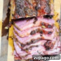 Sliced corned beef roast, featuring a charred exterior and a pink, glazed interior on a wooden cutting board.