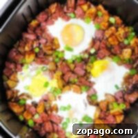 Air Fryer Corned Beef Hash breakfast with eggs, potatoes, and diced meat, topped with sliced green onions.