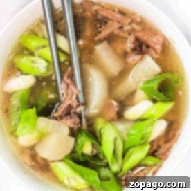 A bowl of Korean Oxtail Soup with green onions and tender meat, paired with chopsticks on a pristine white background.