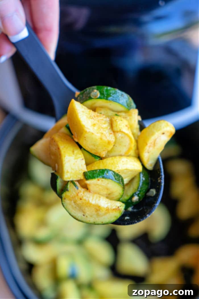 Crispy Air Fryer Squash and Zucchini 6 A spoon lifts air fried zucchini and squash slices, showcasing the vibrant colors of this air fryer squash and zucchini masterpiece above a pot.