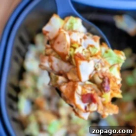 Close-up of a spoon holding savory fried cabbage with crispy bacon pieces, over an air fryer basket.