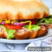 A delicious bundtwich recipe, featuring a large sandwich with turkey, lettuce, tomato, red onion, and peppers, all perfectly nestled on a round bun, beautifully presented on a plate.