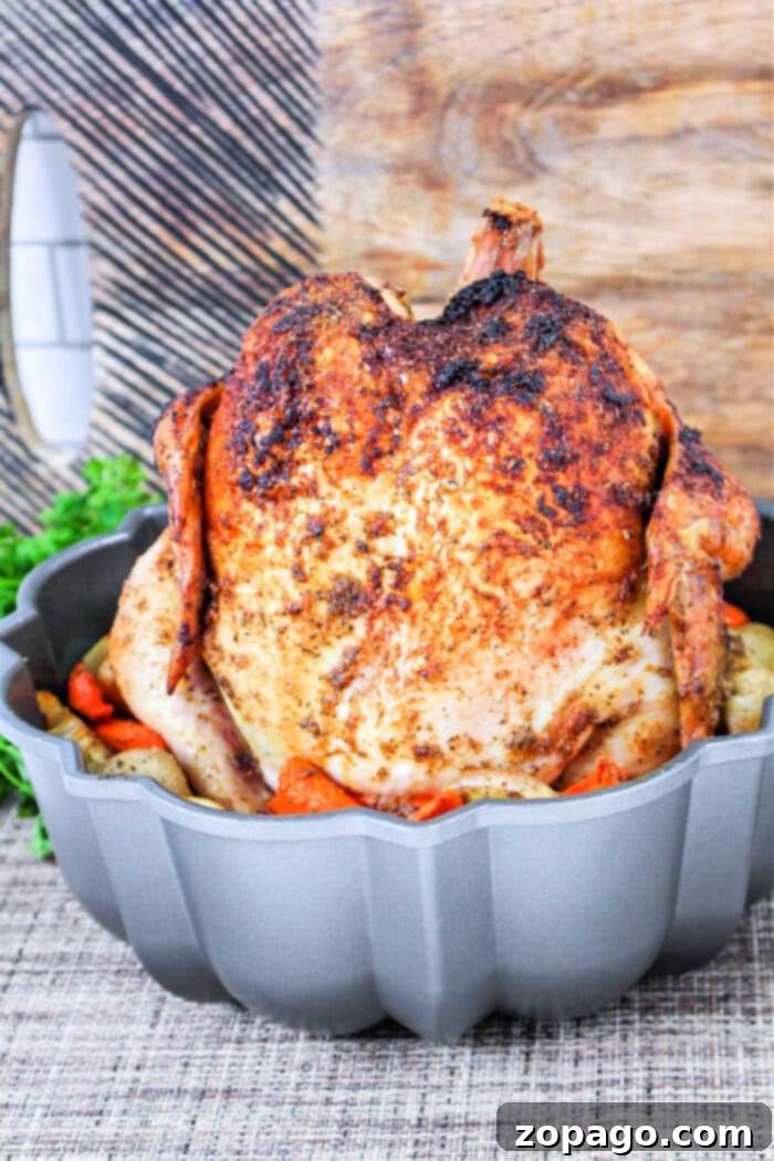Homemade Rotisserie Style Chicken 8 Rotisserie Chicken in Oven: A vibrant full shot of a perfectly roasted chicken standing tall in a Bundt pan, surrounded by colorful, roasted root vegetables.