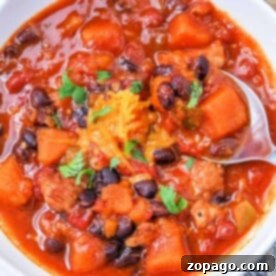 A bowl of Sweet Potato Chili with black beans, chunks of vegetables, cheese, cooked to perfection in an Instant Pot and garnished with parsley.