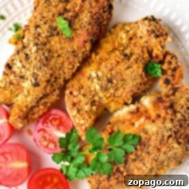 Three almond-crusted chicken breasts on a plate with sliced cherry tomatoes and a parsley garnish.