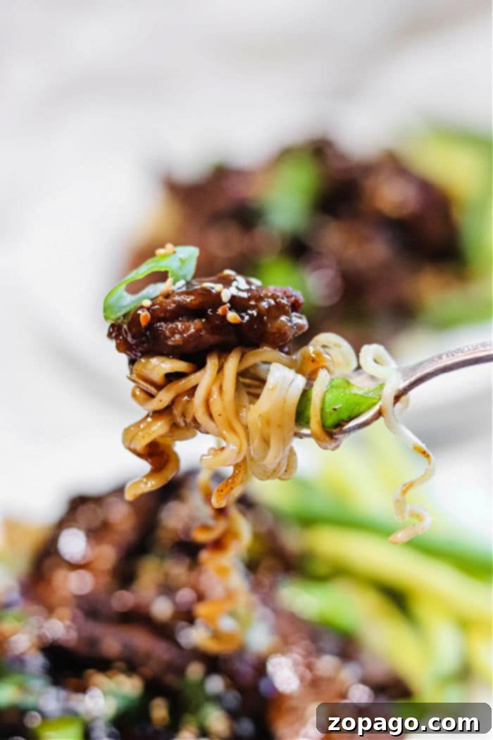 Air Fryer Mongolian Beef 2 Close-up of a fork holding air fryer beef and noodles, sprinkled with sesame seeds and garnished with fresh green onions.