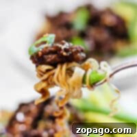 Close-up of a fork holding air fryer beef and noodles, sprinkled with sesame seeds and garnished with fresh green onions.