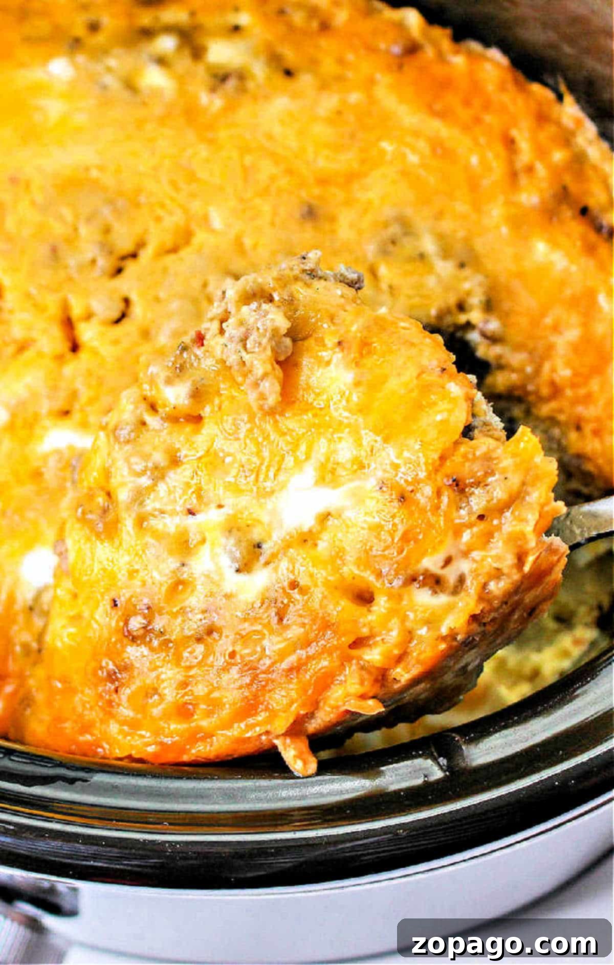 Effortless Slow Cooker Breakfast Scramble 2 A serving spoon lifting a generous portion of fluffy, cheesy scrambled eggs with savory sausage from a slow cooker, highlighting the comforting and easy nature of Crockpot scrambled eggs.
