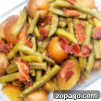 Savory Green Beans with Ham 7 Glass dish featuring vibrant green beans with ham and tender small potatoes, sprinkled with crispy bacon pieces.