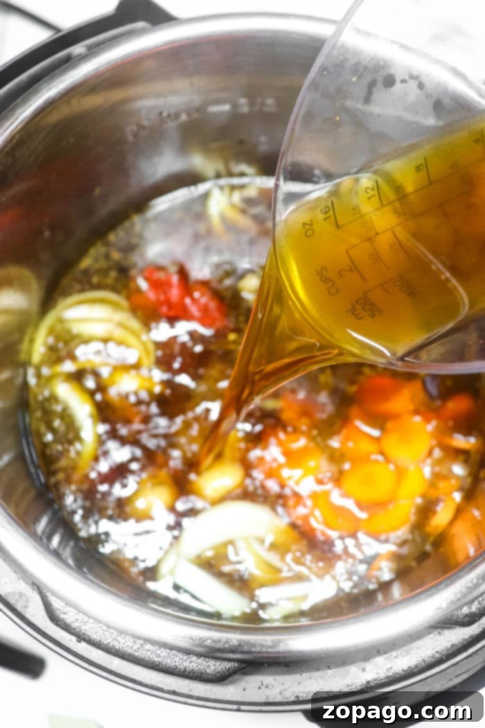 Hearty Instant Pot Oxtail Soup 7 A steady stream of rich beef broth being poured into an Instant Pot, where aromatic sliced onions, carrots, and perfectly seared oxtail await, signifying the beginning of a flavorful oxtail soup.