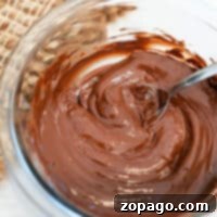 A bowl of velvety melted chocolate, crafted from melting chocolate chips in the microwave, sits invitingly with a spoon on a woven table mat.