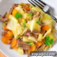 A plate of cabbage stew, featuring tender cabbage, carrots, and shredded meat garnished with parsley, with a fork on the side.