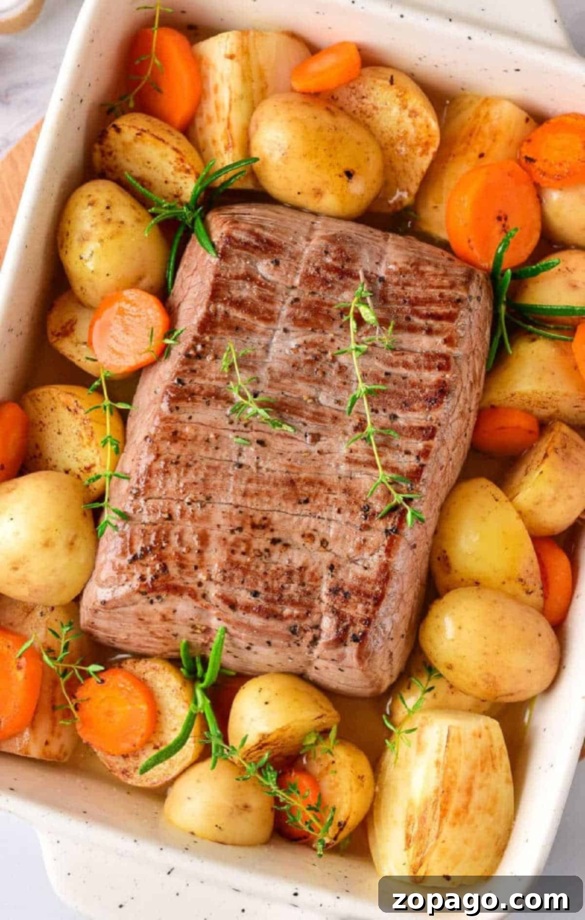 Hearty Oven Chuck Roast 4 Roast beef with potatoes, carrots, and herbs in a white baking dish—perfect for learning how long to cook chuck roast in oven at 350 for a tender, flavorful meal.
