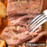 Close-up of a fork shredding tender roast beef with potatoes and carrots in the background—perfect results when you know how long to cook chuck roast in oven at 350 degrees.