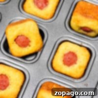 Mini corndog muffins, also known as Corn Dog Bites, nestle in a baking tray, each with a small hot dog snugly in the center.