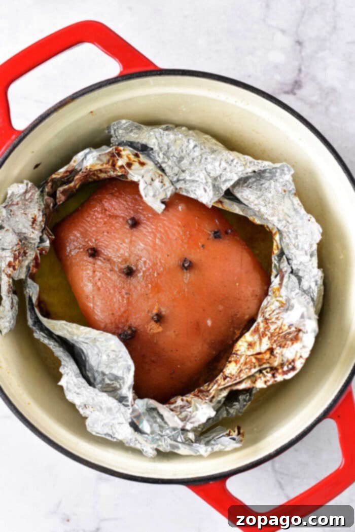 Easy Oven-Roasted Pork Perfection 2 pork roast with cloves wrapped in foil, nestled in a red-handled pot on a marble countertop, evokes the warmth of knowing just how long to cook pork roast in the oven at 375 for that perfect dinner.