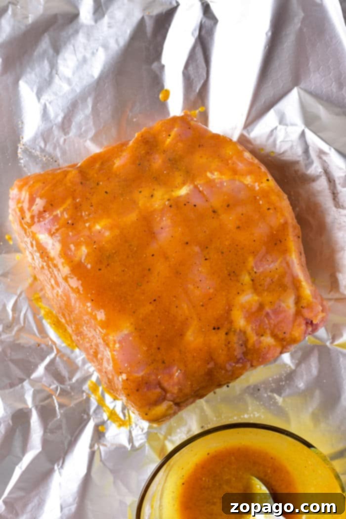 Easy Oven-Roasted Pork Perfection 6 Raw pork roast coated in a bright mustard marinade sits on aluminum foil, with a bowl of the marinade beside it, ready to be transformed just like learning how long to cook a pork roast in the oven at 375 degrees