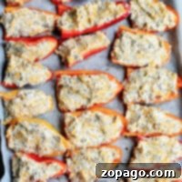 Stuffed mini sweet peppers are halved and laid out on a baking sheet, topped with a delightful mixture of cheese and herbs. These vibrant treats are carefully arranged in rows on parchment paper.