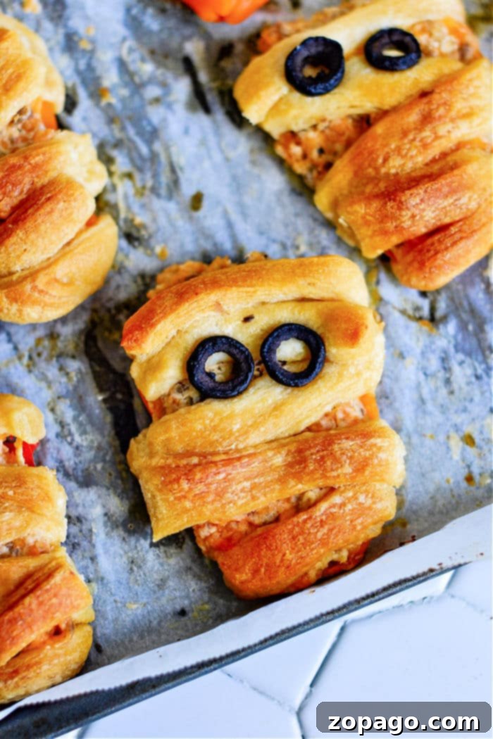 Mini Stuffed Sweet Peppers 7 Freshly baked crescent roll mummies and stuffed mini sweet peppers rest on a parchment-lined baking sheet, the mummies shaped with olive slice eyes and wrapped dough for that classic bandage look.