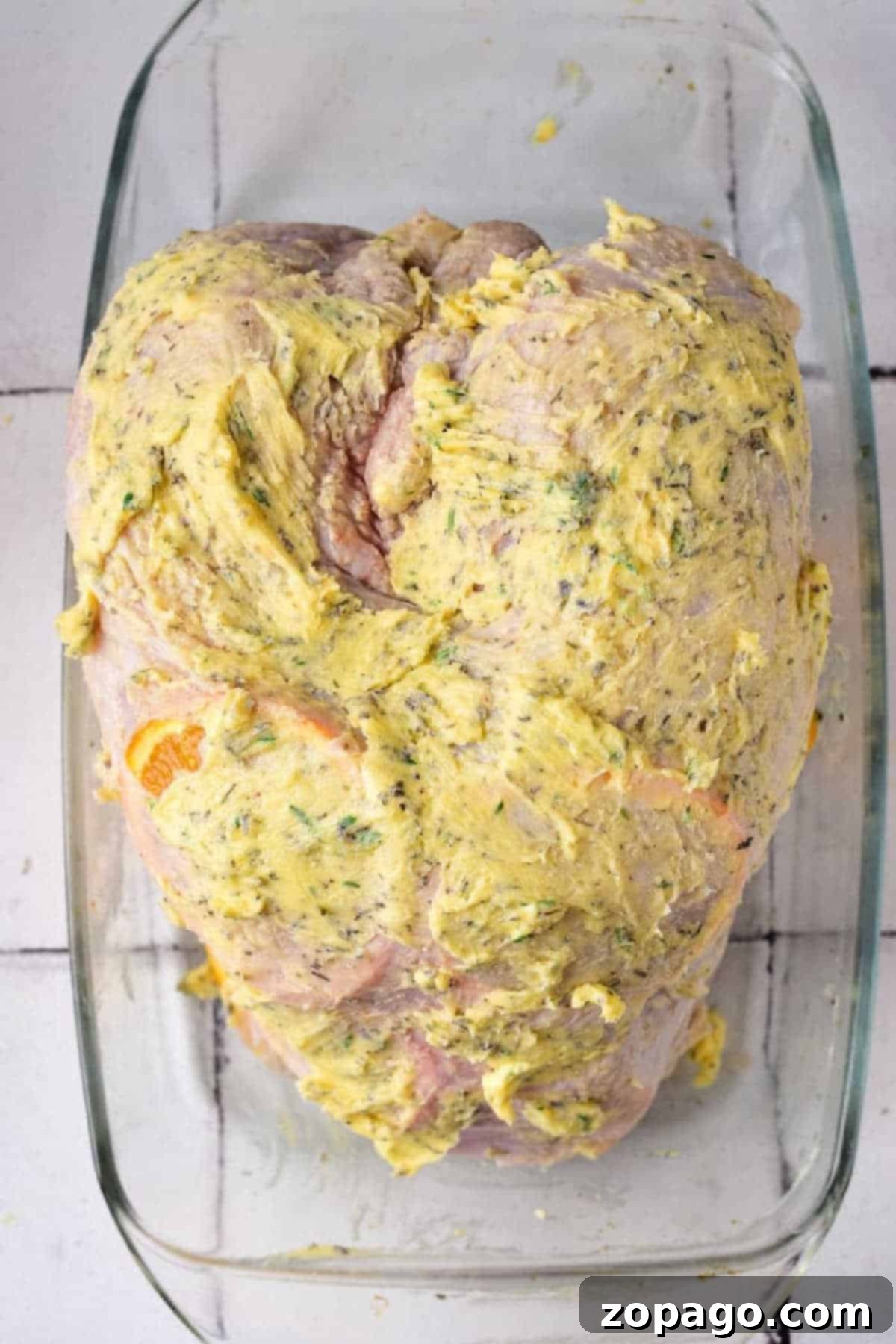 Royal Turkey Roast 4 Raw Turkey Crown coated with a yellow herb butter mixture in a glass baking dish.